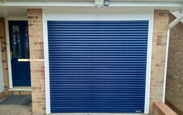 A blue roller door installed on a brick wall, with a portion of a doorway visible to the left.