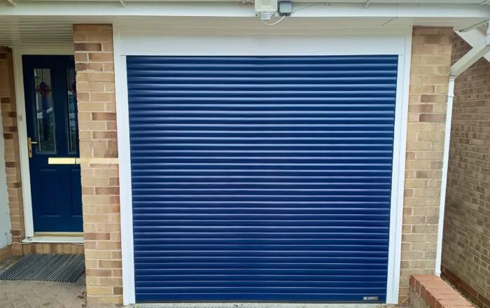 A blue roller door installed on a brick wall, with a portion of a doorway visible to the left.