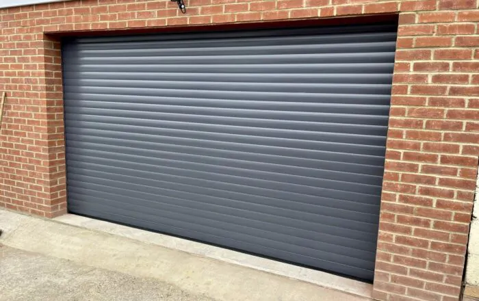 A grey roller garage door set into a brick wall, with a concrete floor below.