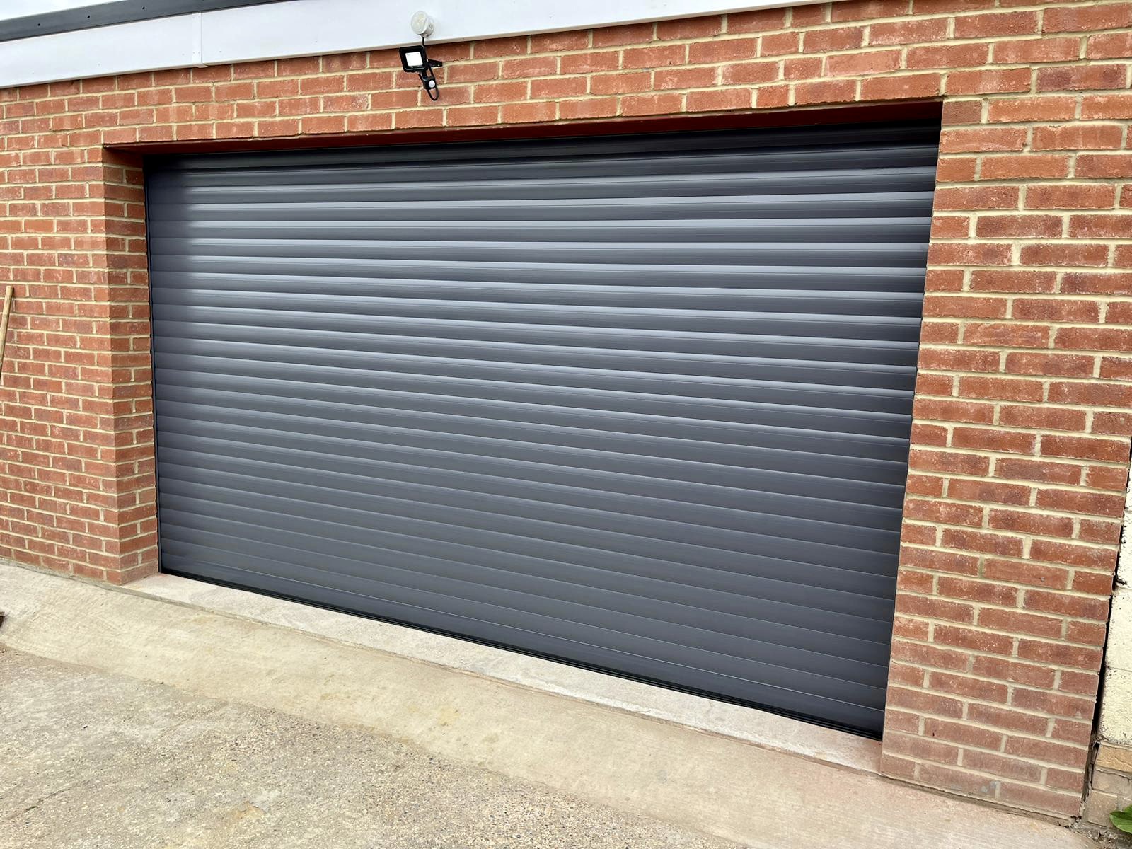 A grey roller garage door set into a brick wall, with a concrete floor below.