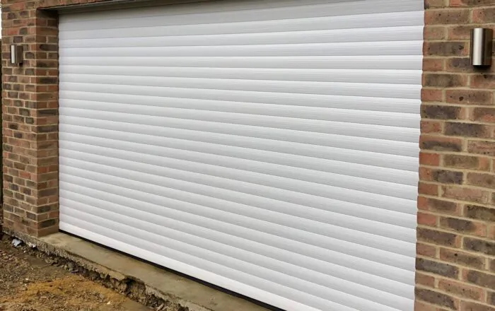 A closed white roller shutter garage door against a brick wall.