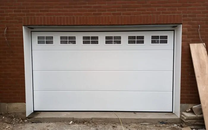 A white garage door with windows, set against a brick wall. There are construction materials nearby.