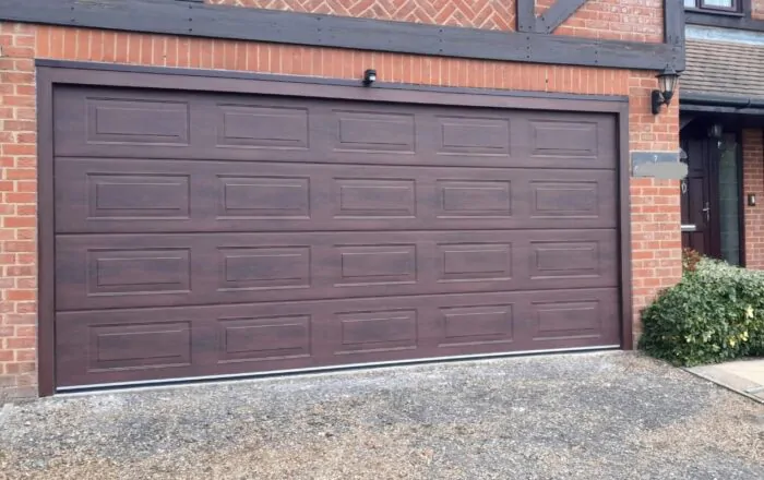 A brown garage door with horizontal panels, set against a brick wall.
