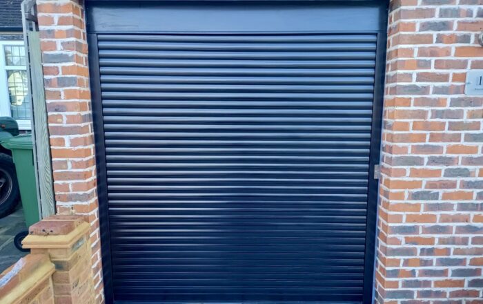A closed black roller garage door with a brick wall surrounding it.