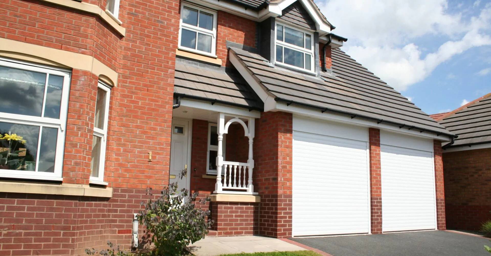 Front view of a residential property with a white roller garage door and a neatly landscaped garden.