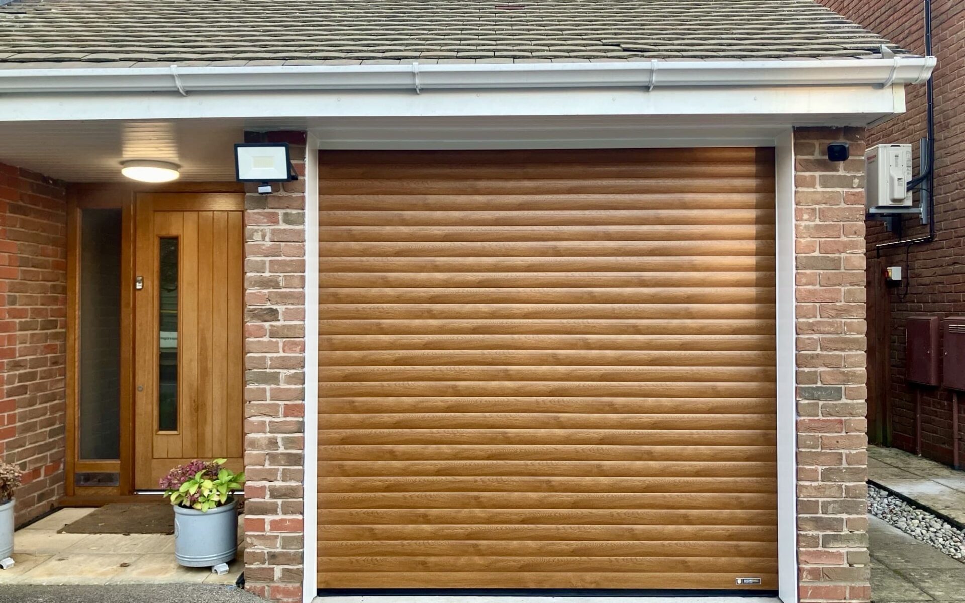 A brown roller garage door, a wooden front door, and potted plants.