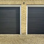 Two black garage doors with horizontal panels, situated next to each other, set against a brick wall.
