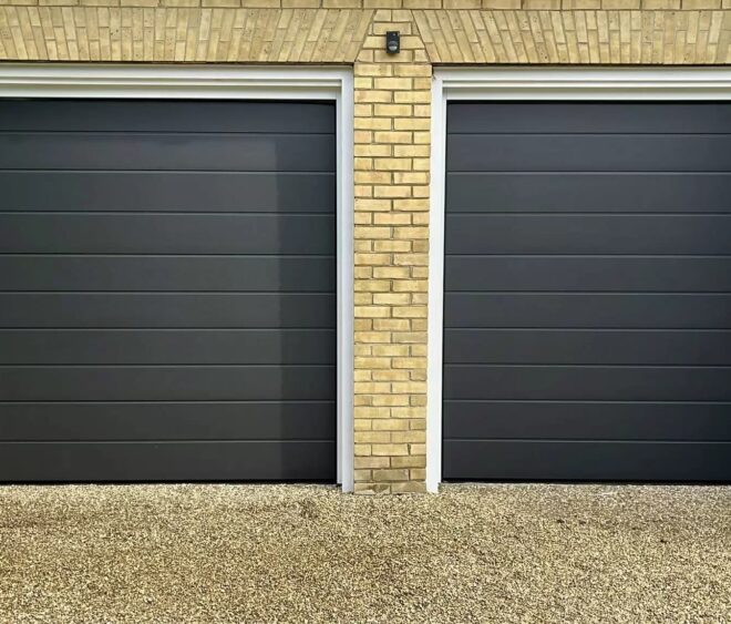 Two black garage doors with horizontal panels, situated next to each other, set against a brick wall.