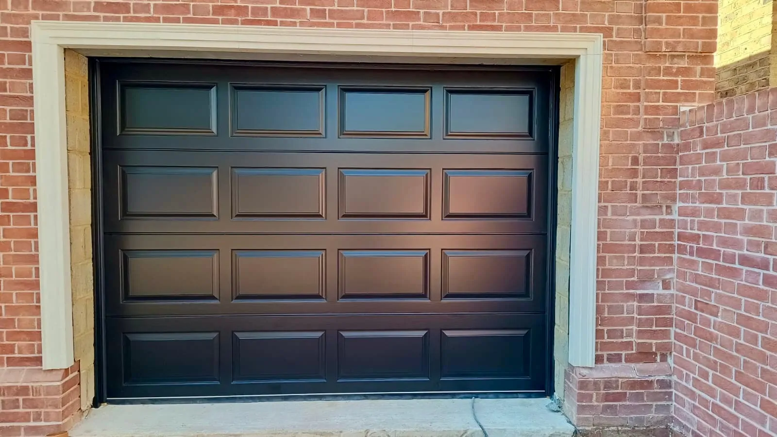 A black garage door with a panel design, set in a brick wall.