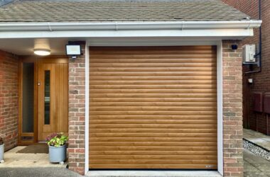 A brown roller garage door with horizontal slats, adjacent to a wooden front door and brick wall.