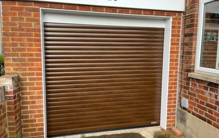 A brown automated roller garage door with horizontal slats, set within a brick wall.