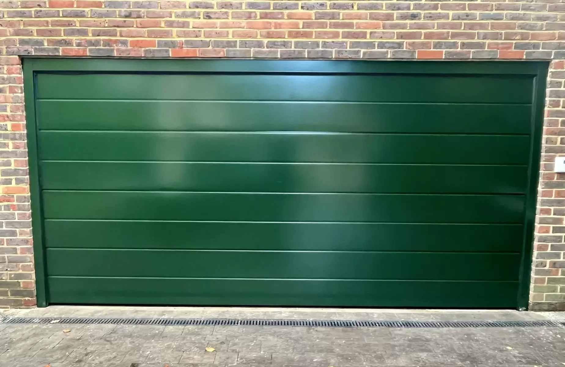A green, horizontal slatted garage door set against a brick wall.