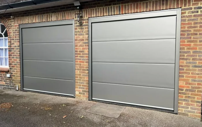 Two grey garage doors with horizontal lines, set against a brick wall.